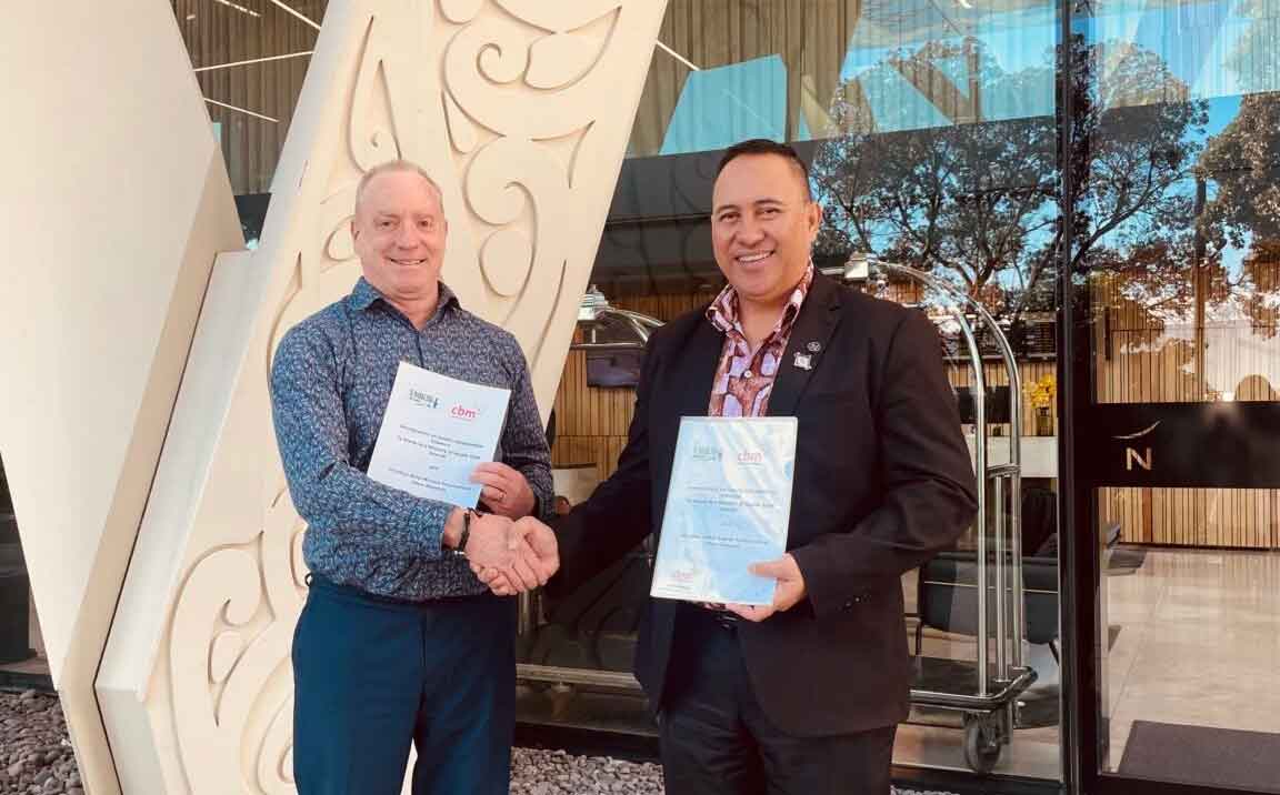 Dr Murray Sheard of cbm New Zealand and Te Marae Ora Secretary of Health Bob Williams shake hands, each holding a signed copy of the partnership agreement.